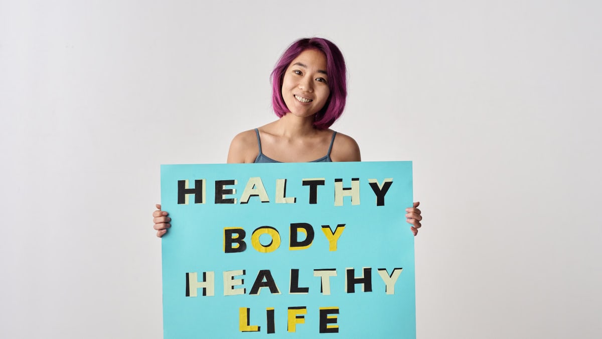 A young woman with purple hair holding a poster promoting a healthy lifestyle.